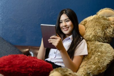 Portrait of Asian student in university uniform using a tablet computer in the living room after studying at the university. Lifestyle,Education, technology and internet concept.